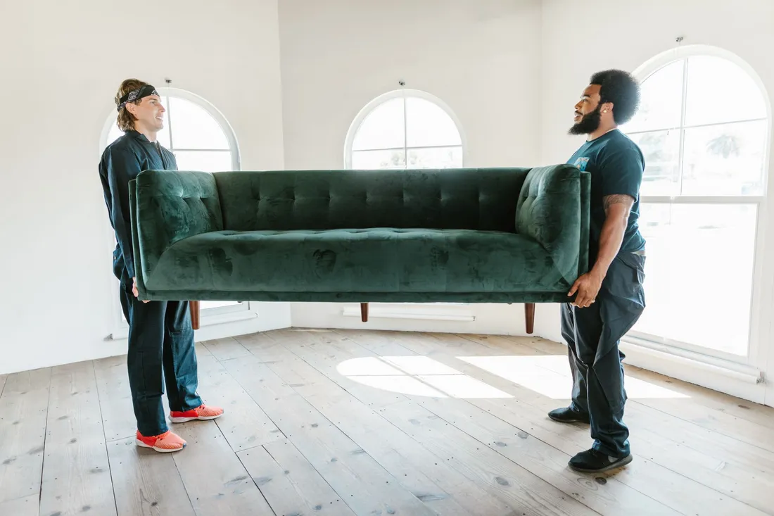 Zwei Umzugshelfer tragen ein Sofa aus einem Hauseingang